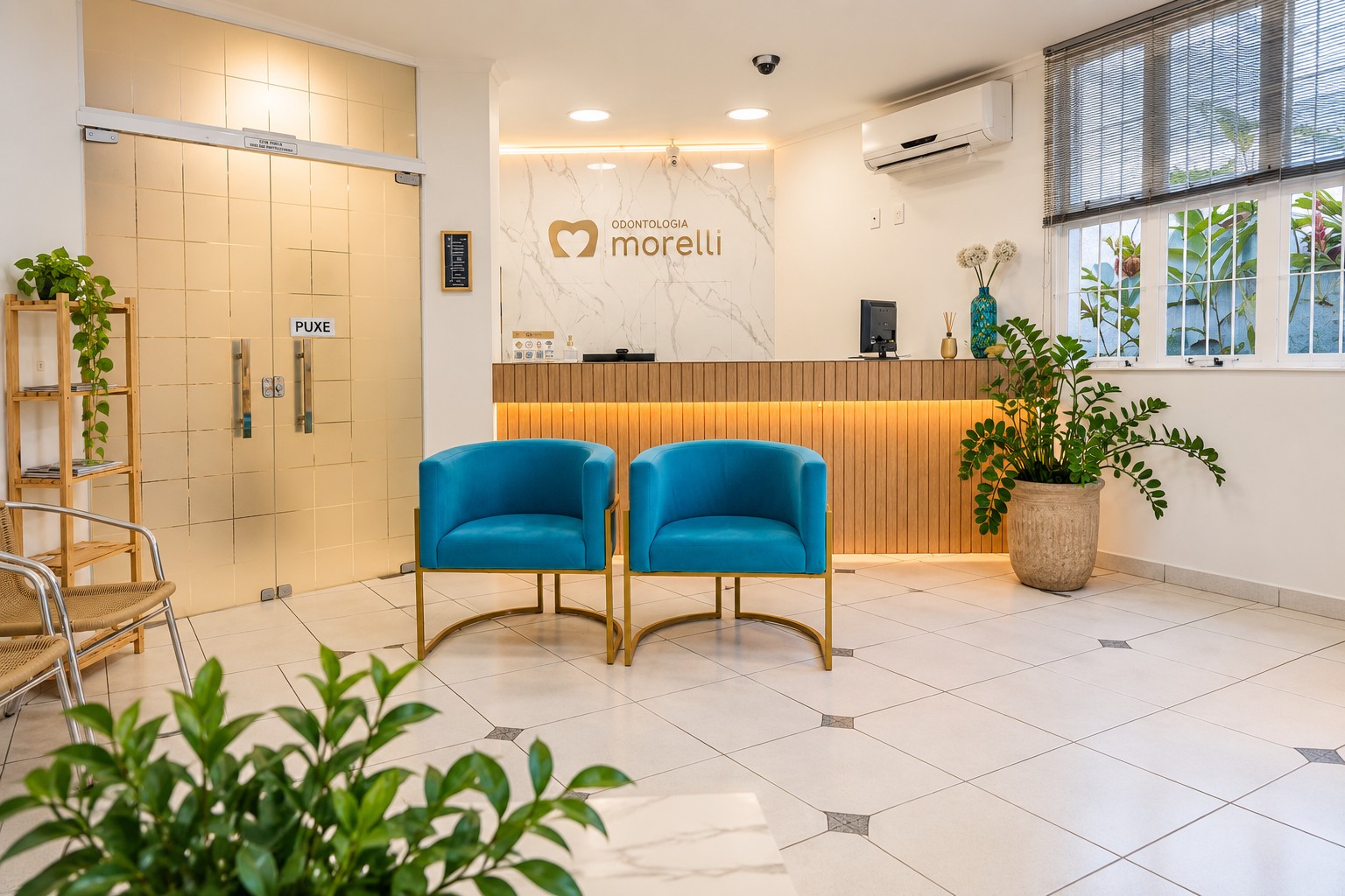 Recepção da Odontologia Morelli, com balcão iluminado, parede com a marca e poltronas azuis